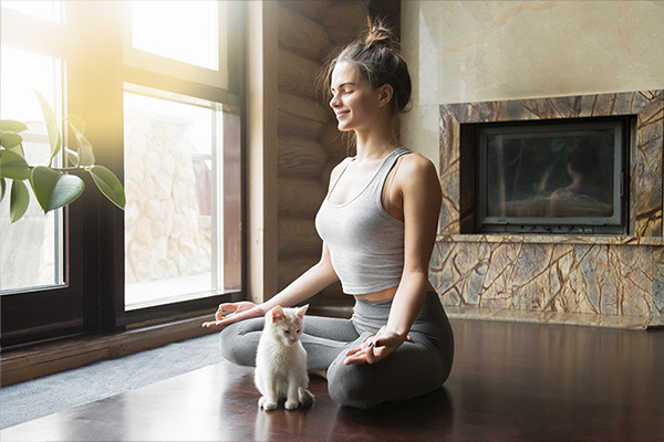 Girl smiling sat on floor crossed legged in yoga pose with a kitten by her lap